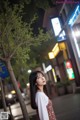 A woman standing next to a tree on a city street.