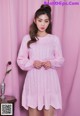 a woman wearing a pink sweater dress standing in front of a pink curtain