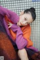 A woman in a purple and orange sweater sitting on a bed.