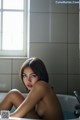 A naked woman sitting in a bathtub in a bathroom.