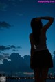 A woman standing in front of a body of water at night.