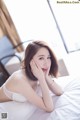 A woman laying on top of a bed in a white bra.