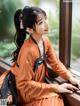 A woman in an orange dress sitting by a window.