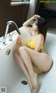 A woman in a yellow lingerie sitting in a bathtub.