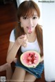 A young woman eating a slice of watermelon with a spoon.