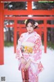 A woman in a pink kimono standing in front of a red gate.