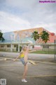 A woman in a yellow tank top and denim shorts doing a handstand.