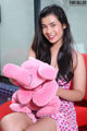 A woman sitting on a red couch holding a pink stuffed animal.