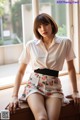 A woman sitting on a window sill wearing a white shirt and floral shorts.