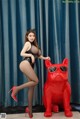 A woman in a black bodysuit and red high heels posing next to a red dog.